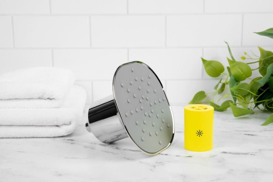 Showerhead and yellow filter next to folded towels and green plant.