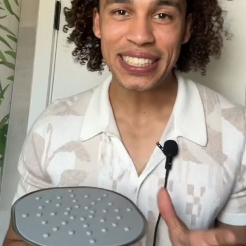 Person smiling and holding a large, round object with a microphone clipped to their shirt.