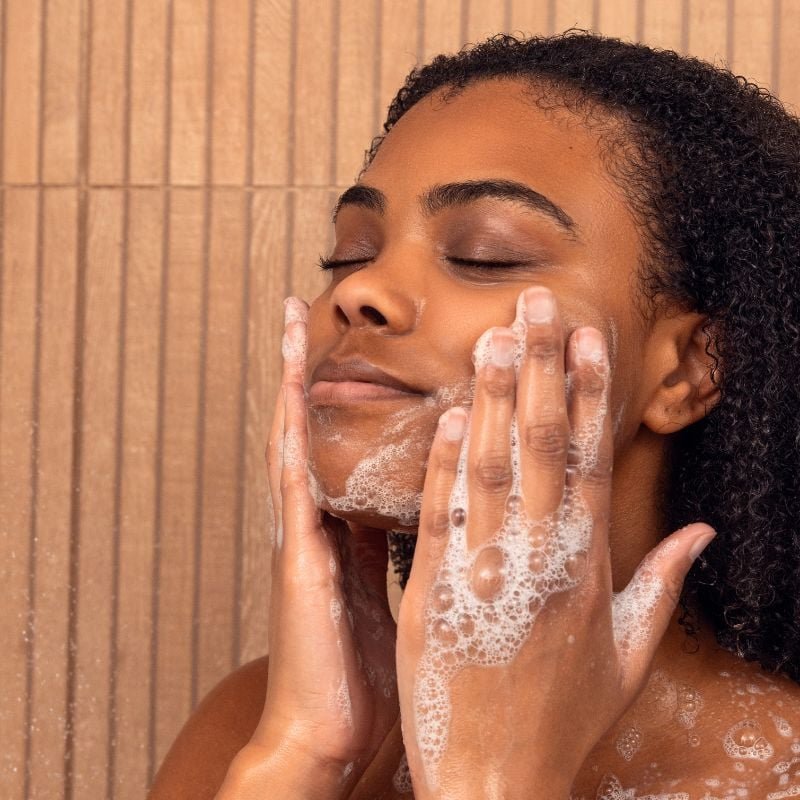 Person washing their face with soap in a shower setting.