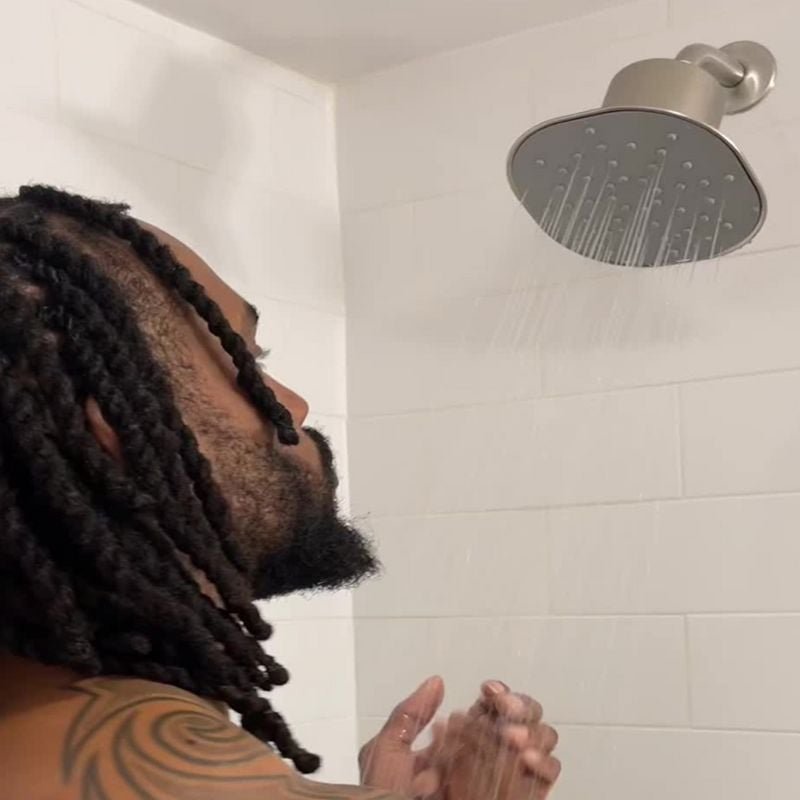 Person with braided hair showering under a modern showerhead.