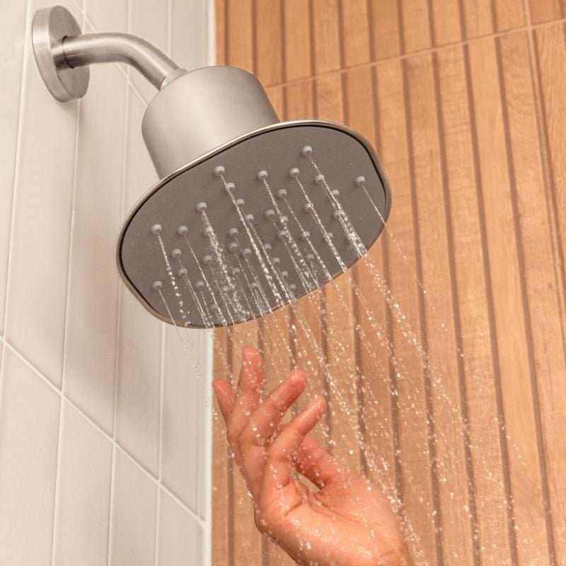 A hand testing the flow of water from a showerhead.